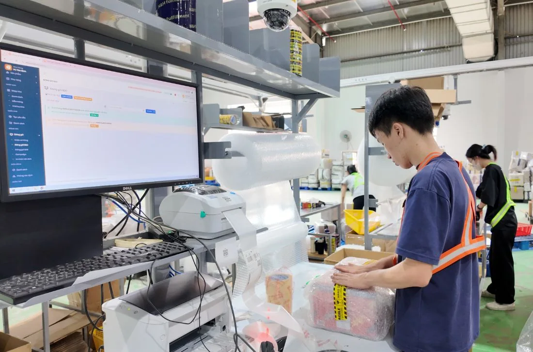 Nhân viên đóng gói đơn hàng tại bàn có màn hình hệ thống OMS trong kho Onflow Fulfillment